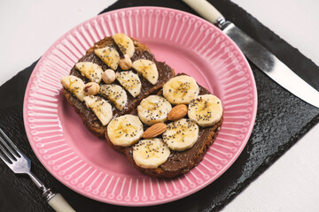 Toasted whole wheat bread with chocolate nuts paste nutella topping, banana, chia seeds, almonds and hazelnuts toast. Healthy proper nutrition for breakfast
