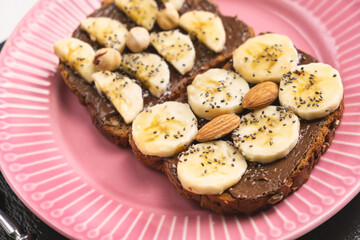 Toasted whole wheat bread with chocolate nuts paste nutella topping, banana, chia seeds, almonds and hazelnuts toast. Healthy proper nutrition for breakfast