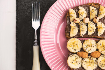 Toasted whole wheat bread with chocolate nuts paste nutella topping, banana, chia seeds, almonds and hazelnuts toast. Healthy proper nutrition for breakfast