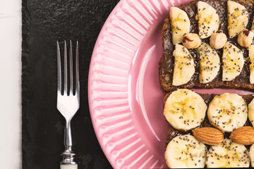 Toasted whole wheat bread with chocolate nuts paste nutella topping, banana, chia seeds, almonds and hazelnuts toast. Healthy proper nutrition for breakfast
