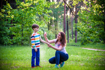 Young woman mother applying insect repellent to her son before forest hike beautiful summer day or evening. Protecting children from biting insects at summer. Active leisure with kids.