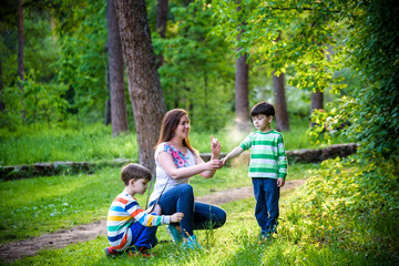 Young woman mother applying insect repellent to her two son before forest hike beautiful summer day or evening. Protecting children from biting insects at summer. Active leisure with kids