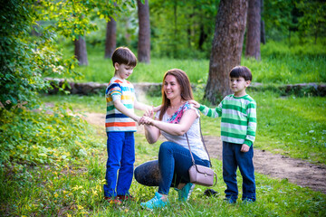 Fototapeta premium Young woman mother applying insect repellent to her two son before forest hike beautiful summer day or evening. Protecting children from biting insects at summer. Active leisure with kids