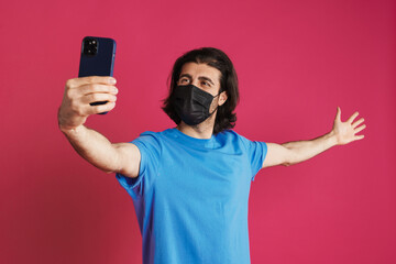 White man in face mask taking selfie on cellphone and showing copyspace