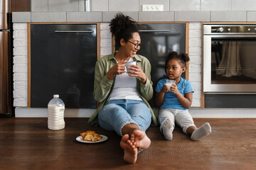 Happy mother sitting on floor with her daughter in home kitchen
