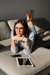 Fototapeta premium Young white woman lying on sofa with tablet computer and cellphone