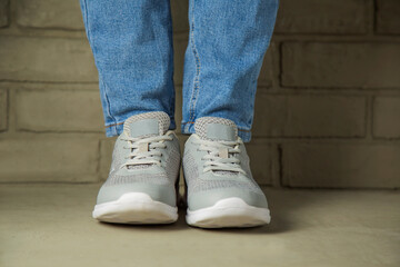 A woman in white sneakers stands against a brick wall in the background.