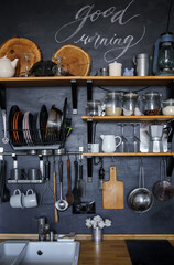 modern home kitchen design in loft and rustic style. black wall with shelves, trays, cans, mugs, coffee maker and sink. Inscription Good morning.