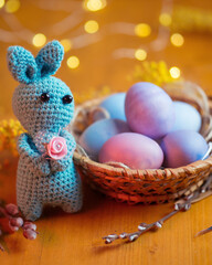Easter bunny and basket with painted pastel Easter eggs on a wooden table, bokeh garland