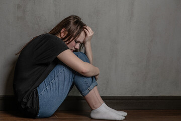 Unhappy teen girl sits on the floor near a wall. Empty space for text