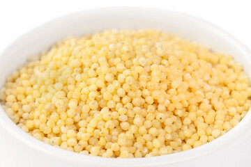 Raw dried uncooked millet seeds with white ceramic plate macro