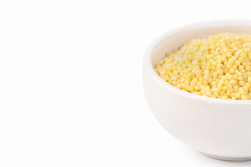 Raw dried uncooked millet seeds with white ceramic plate place for text and light background macro