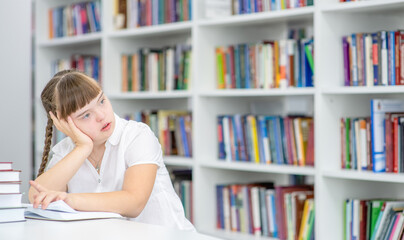 Pensive girl with syndrome down sits at library. Empty space for text. Education for disabled children concept