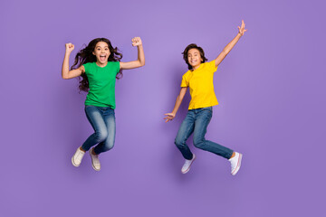 Fototapeta na wymiar Full length photo of two excited kids happy smile celebrate win victory girl fists hands jump up isolated over purple color background