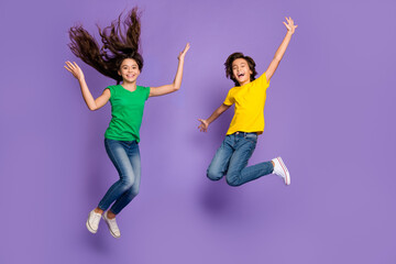 Full length photo of brother and sister jump up fly hair wear t-shirt jeans isolated on violet color background