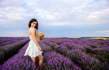 Portrait of a young woman in white dress and straw hat walking in the lavender field