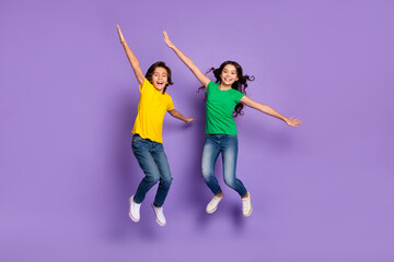 Full size photo of brunette happy kids jump hands wings wear t-shirt jeans isolated on purple color background