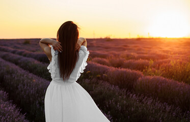 Fototapeta na wymiar Back view of a young woman in white dress walking in the lavender field.