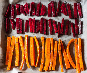 A healthy snack on the right diet. Fresh carrots and beets, cut into strips in spices, are laid out on parchment on a baking sheet