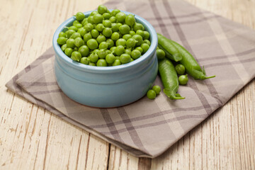 Green peas in bowl on gray cotton napkin and wooden background