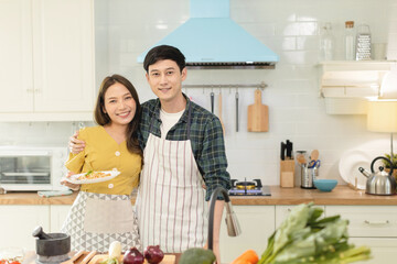 Portrait young couple in love helping to cook In a romantic atmosphere at home and looking at camera with smile face.