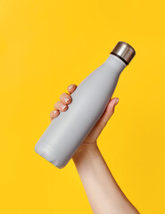 Hand with grey reusable insulated bottle on yellow background