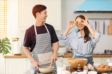 Asian couple Help each other to make a bakery In a romantic atmosphere in the kitchen at home. Young women help cook holiday with smiling and happy faces.