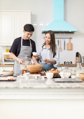 Asian couple Help each other to make a bakery In a romantic atmosphere in the kitchen at home. Young people work together to mix the ingredients in a wooden bowl before stirring them together.