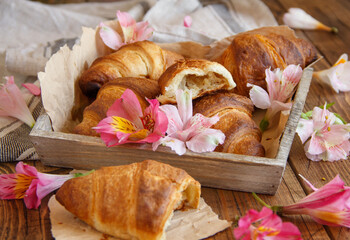 Fresh croissants and flowers in a tray on a wooden table