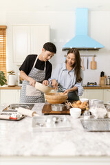 Asian couple Help each other to make a bakery In a romantic atmosphere in the kitchen at home. Young people work together to mix the ingredients in a wooden bowl before stirring them together.
