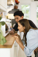 Asian couple Help each other to make a bakery In a romantic atmosphere in the kitchen at home. Young people are watching a cake made with an excited and happy face.