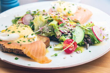 Two delicious poached eggs with salmon on toast served with mixed vegetables and lettuce in white ceramic plate