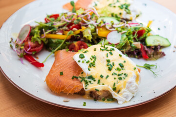 Two delicious poached eggs with salmon on toast served with mixed vegetables and lettuce in white ceramic plate
