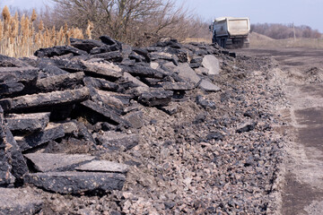 A pile of old black asphalt near the road. A dump truck involved in road repairs.