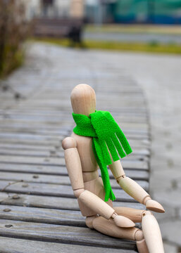 Gestalta figure in green scarf sitting in park bench. Doll gestalta as symbol of sadness, loneliness, illness