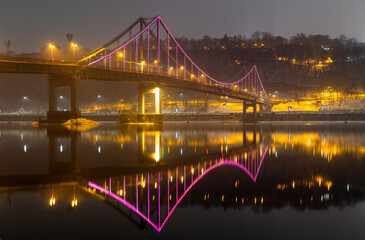 Obraz premium Pedestrian bridge in Kiev. Evening lighting. Reflection of the bridge in the river.