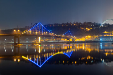 Pedestrian bridge in Kiev. Evening lighting. Reflection of the bridge in the river.