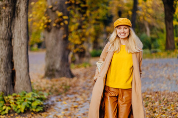 Season and people concept. Beautiful happy young blond woman having fun, enjoying bright colors and walking in autumn park.