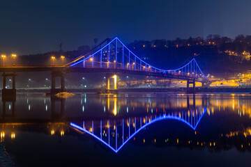 Pedestrian bridge in Kiev. Evening lighting. Reflection of the bridge in the river.