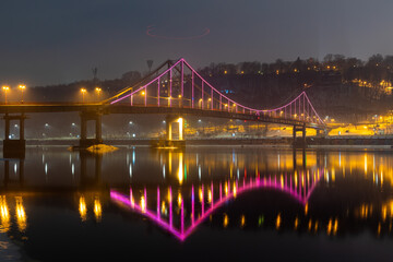 Pedestrian bridge in Kiev. Evening lighting. Reflection of the bridge in the river.
