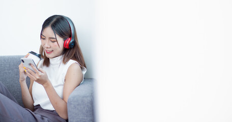 Beautiful young asian woman with headphones relaxing on the sofa. She is listening to music using...