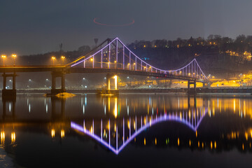 Fototapeta na wymiar Pedestrian bridge in Kiev. Evening lighting. Reflection of the bridge in the river.
