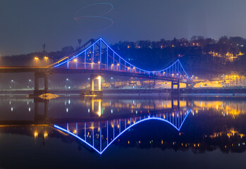 Obraz premium Pedestrian bridge in Kiev. Evening lighting. Reflection of the bridge in the river.