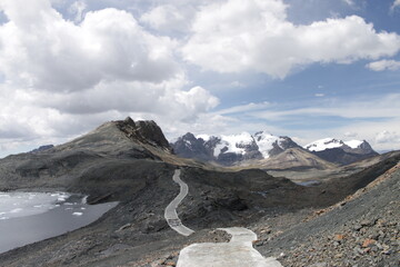 Glacier in huaraz peru, path to the snowy and icy mountains on the horizon, with a lake on the side...