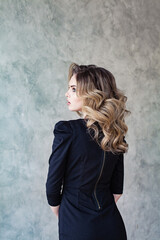 Woman with beautiful healthy curly hairstyle in black dress on gray background portrait