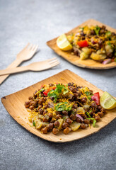 kala chana chaat with boiled potato, onion, tomato with lemon on a bamboo plate 