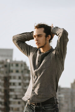 Man walking on the rooftop, wearing casual, curly hair collected in the pony tail. Background of residential building. Urban rooftopper extreme lifestyle, cityscape, abandoned atmosphere
