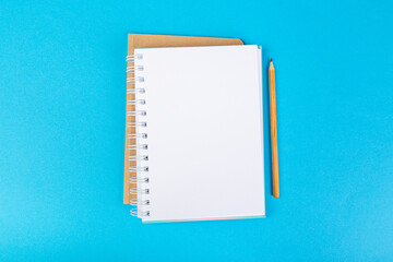 school notebooks on a blue background, spiral notepad with a blank page and a pencil on the table top view