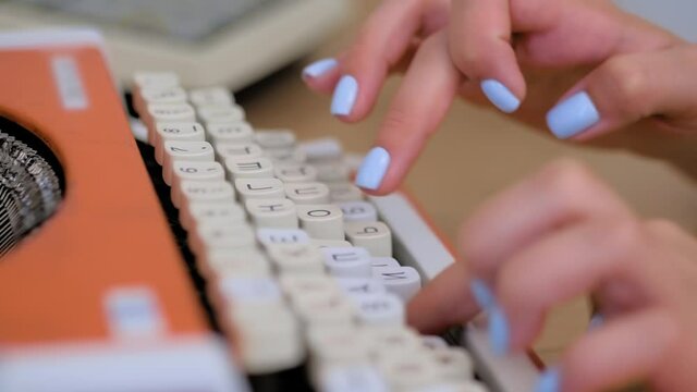 Close up view: woman hands typing on old vintage orange typewriter on table at museum, exhibition. Retro, nostalgia and communication concept