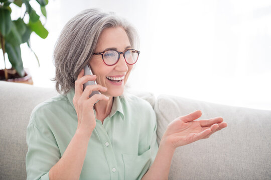 Portrait of satisfied pretty aged person speak phone arm explaining toothy smile have good mood indoors